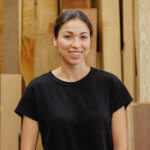 female woodworker with black shirt in front of wood timber