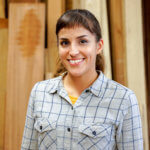 female woodworker with light colored plaid shirt in front of wood timber